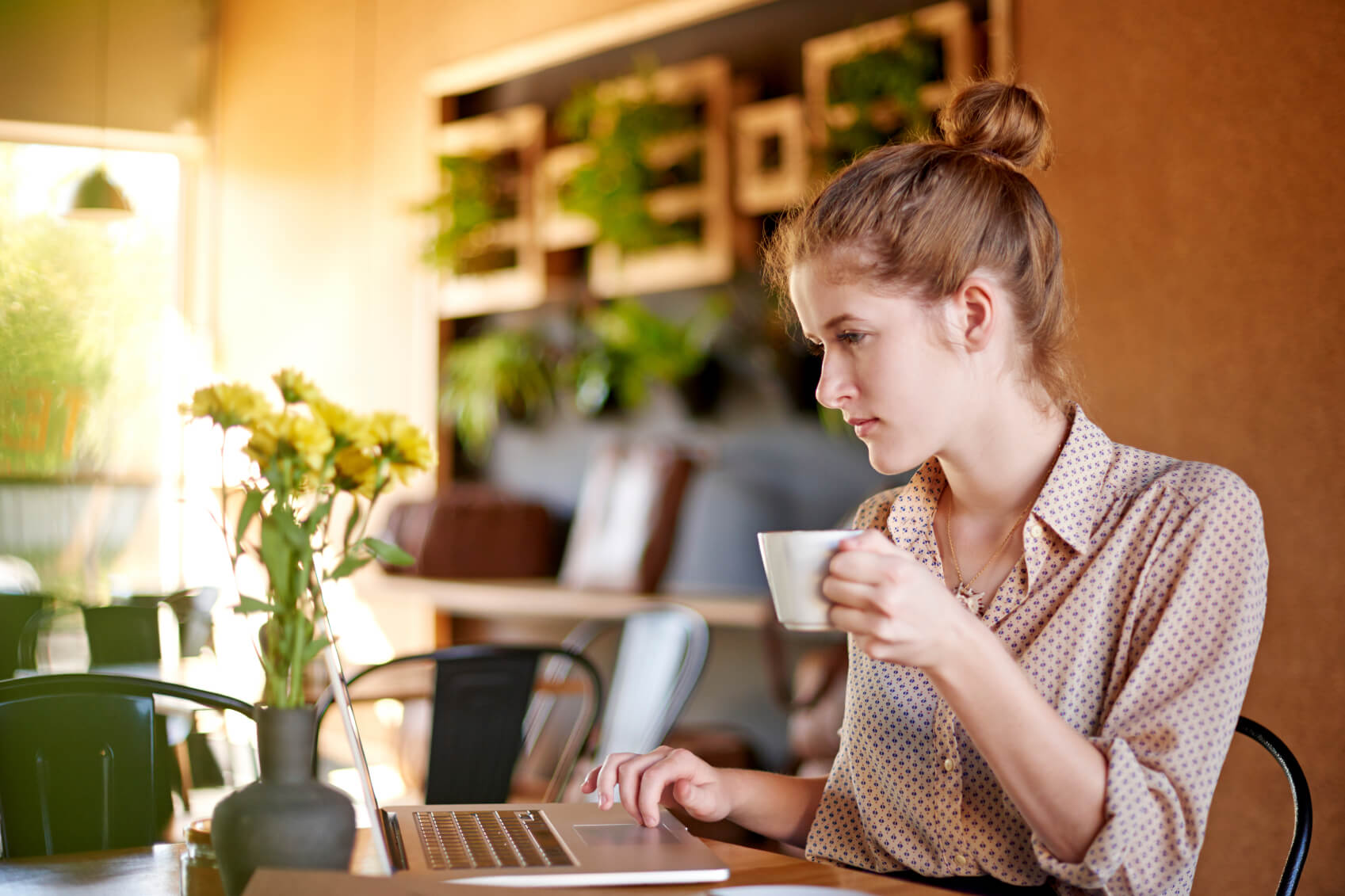 A woman in her 30s sitting in her kitchen and searching for a trusted builder on her laptop